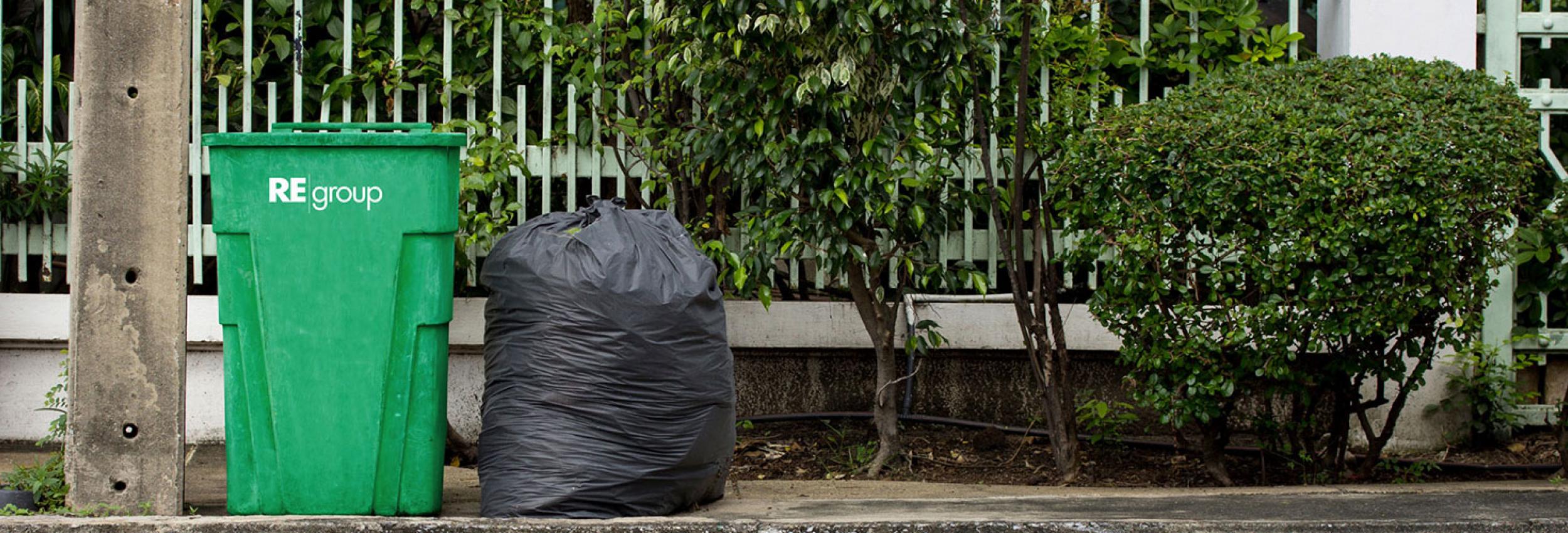 Green bin and garbage bag sitting on the sidewalk.